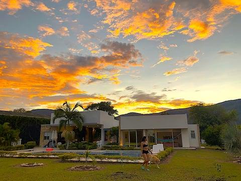 Casa con piscina y jardín tropical al atardecer en Apulo con cielo dorado