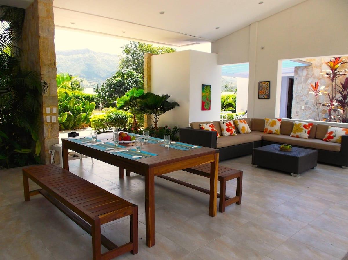 Terraza cubierta con comedor y sala exterior en casa tropical de Apulo con vista a montañas