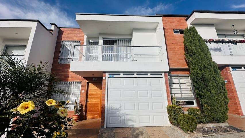 Fachada moderna de casa vacacional en Rionegro con garaje blanco, balcón y jardín con flores amarillas