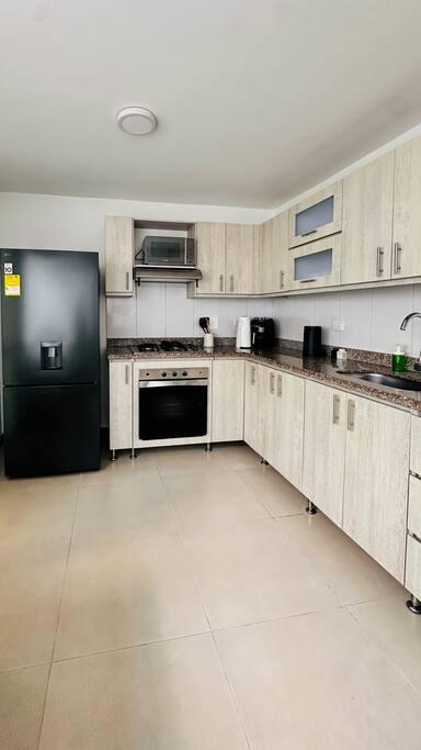Cocina moderna equipada con nevera negra, estufa y gabinetes de madera clara en casa vacacional de Rionegro