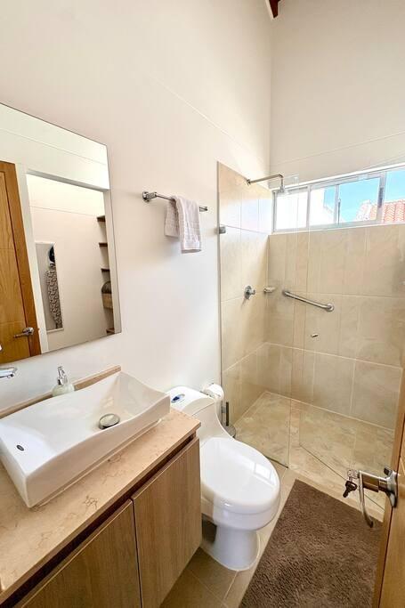 Baño privado moderno con ducha de vidrio, lavamanos vessel y ventana en casa de Rionegro
