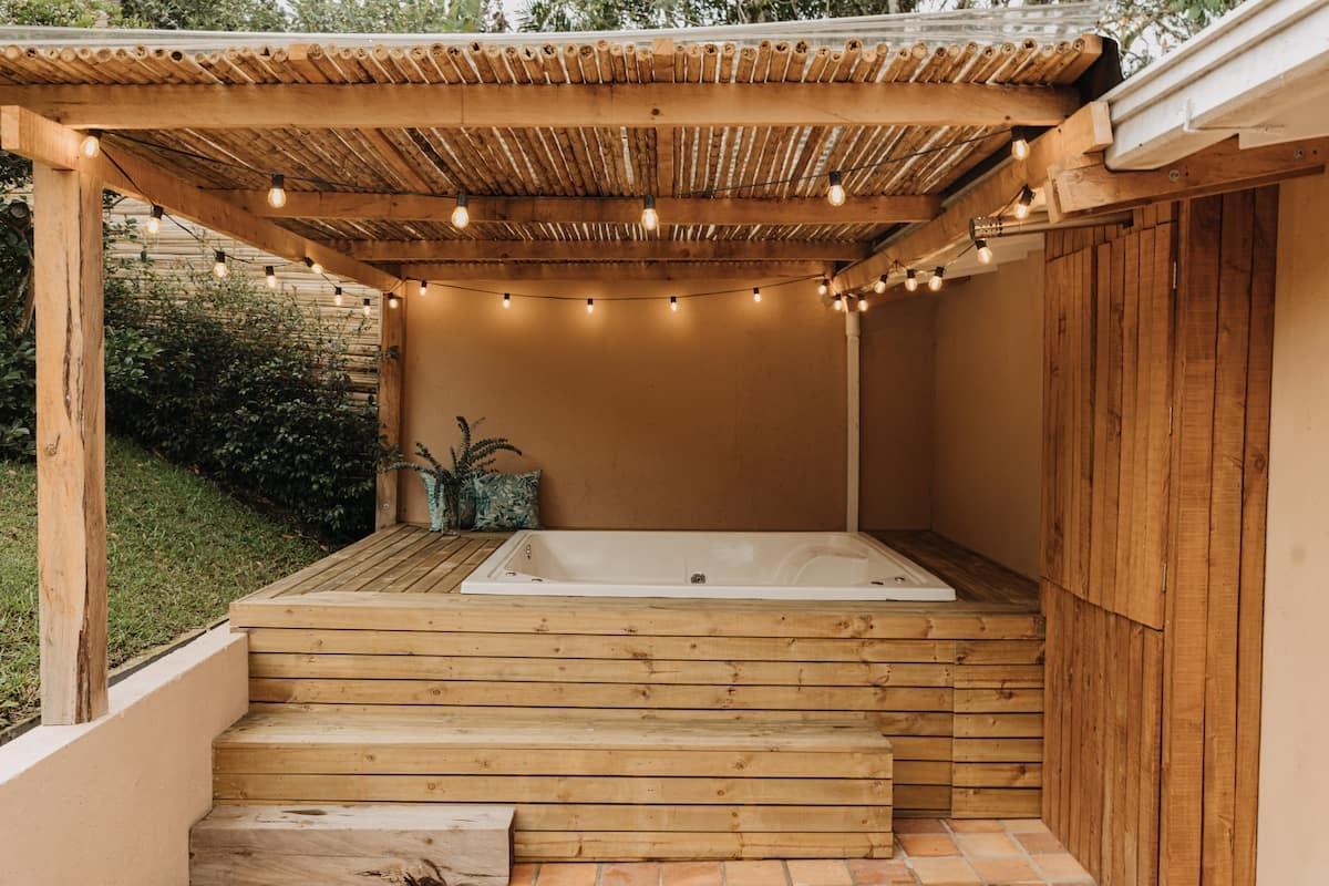 Jacuzzi exterior con deck de madera, pérgola de bambú y luces cálidas en casa de Rionegro