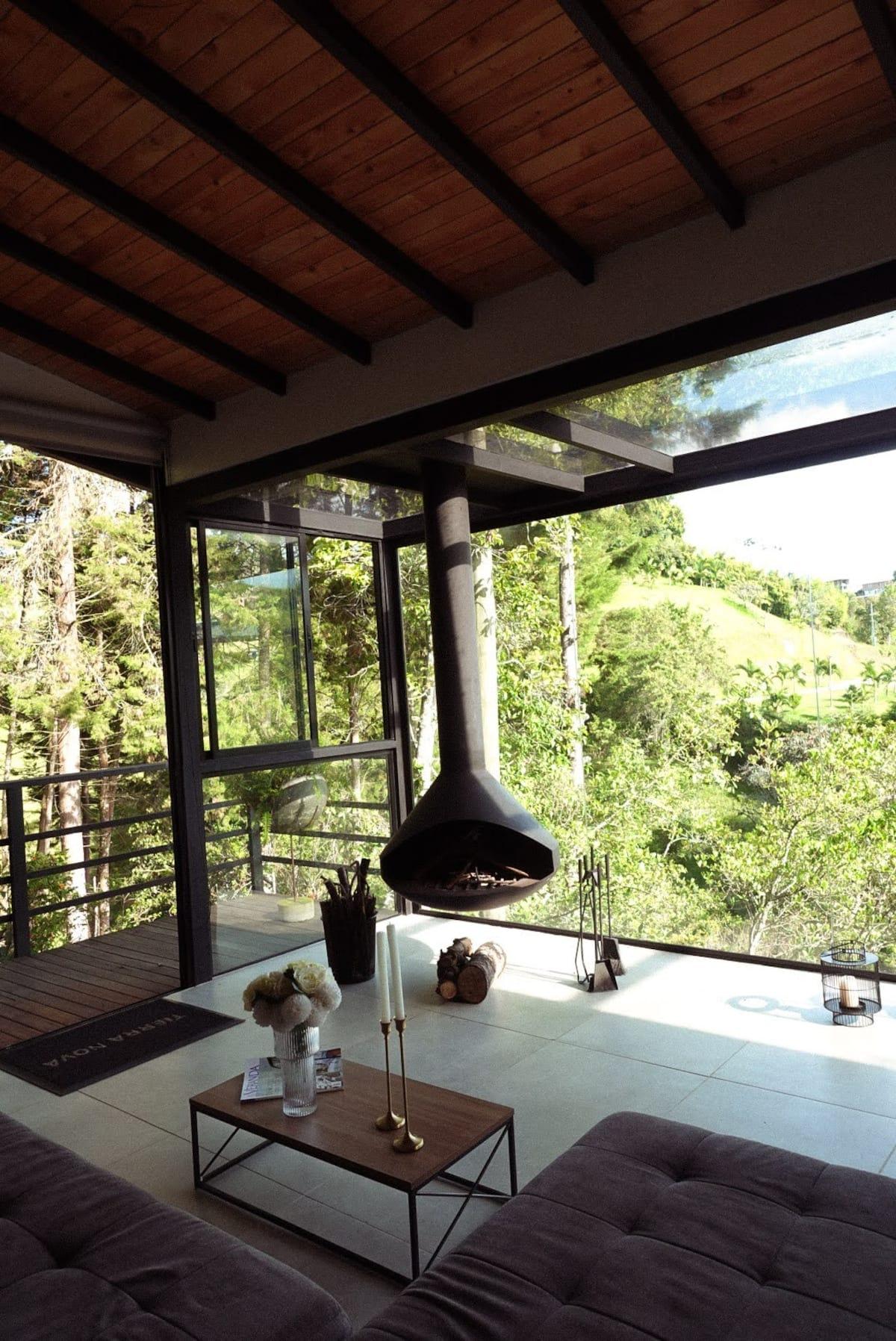 Sala moderna con chimenea colgante y vista panorámica al bosque en casa de Rionegro